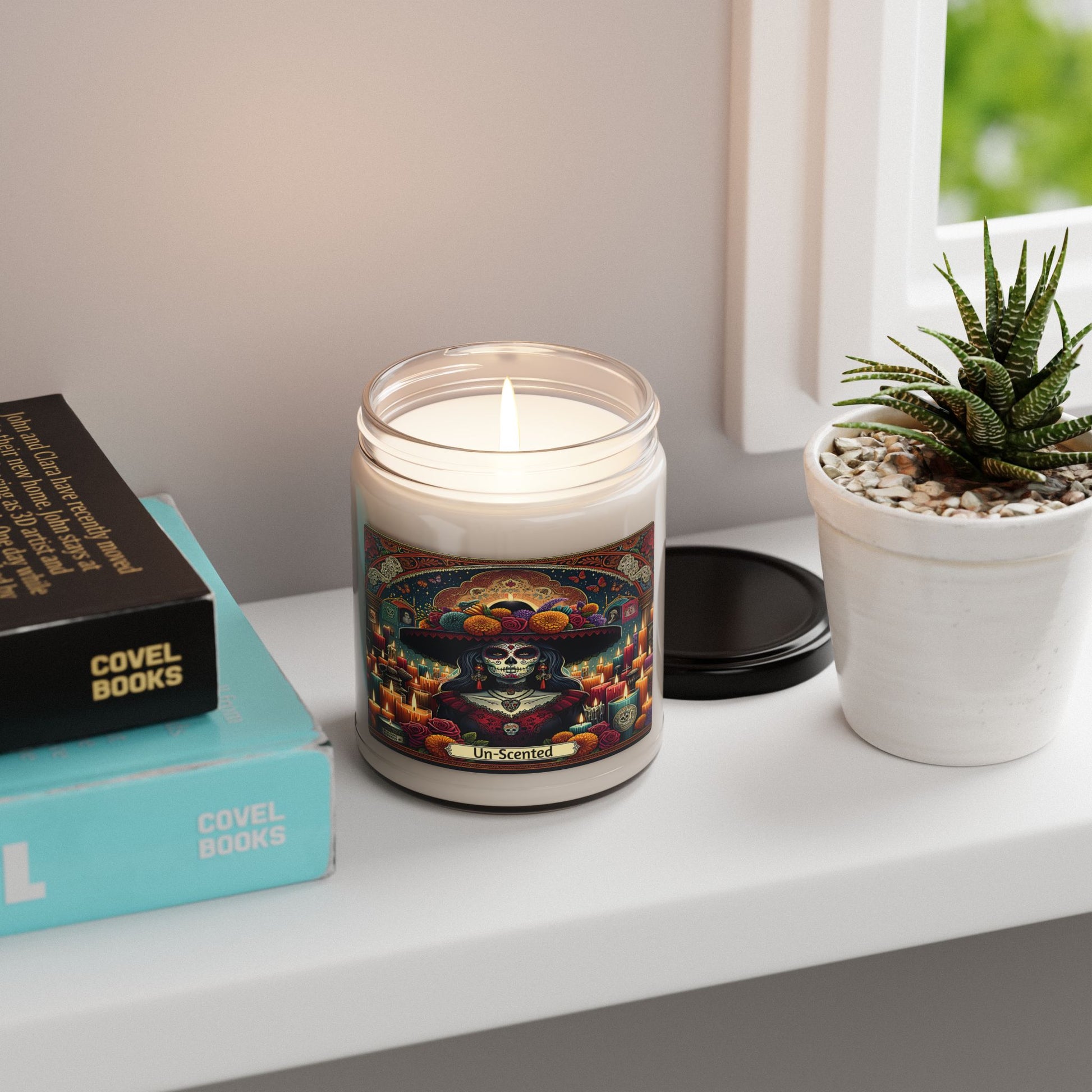Candle with colorful label on a shelf next to books and a plant